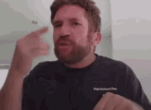 a man with a beard is wearing a black t-shirt and pointing at something .