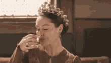 a woman in a tiara is drinking a glass of wine .