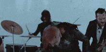 a man in a suit is playing drums and another man is playing guitar