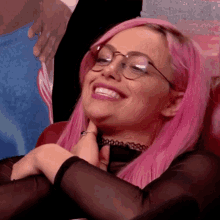 a woman with pink hair wearing glasses and a choker is smiling