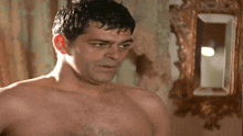a shirtless man stands in front of a mirror looking at himself