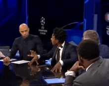 a group of people sitting around a table with champions league written on the wall behind them