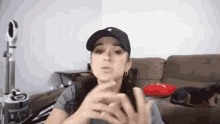 a woman wearing a baseball cap and earrings is sitting on a couch with her hands folded .