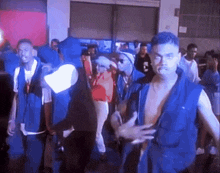 a group of men in blue vests are standing in a room .