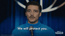 a man in a blue sweater stands in front of a microphone with the words we will protect you behind him