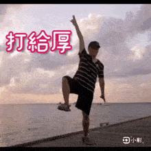 a man in a striped shirt is standing on one leg in front of the ocean ..