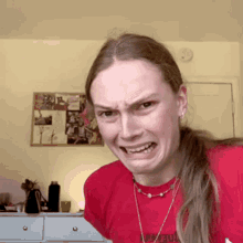 a woman wearing a red t-shirt with a necklace around her neck is making a face