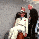 a man in a white suit sits on a suitcase