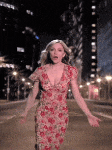 a woman in a red floral dress is walking down a street