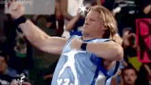 a wrestler in a blue jersey is standing in front of a crowd .