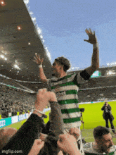 a soccer player wearing a celtic shirt is being lifted in the air by fans