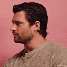 a man with a beard is wearing a grey shirt and looking to the side .