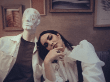 a woman sitting next to a mannequin with a mask on her face