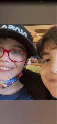 a boy wearing a nasa hat smiles next to another boy wearing glasses
