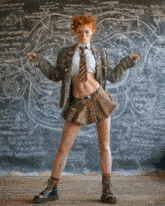 a woman in a plaid skirt and tie stands in front of a chalkboard with a map drawn on it