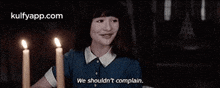 a girl is sitting at a table with three lit candles and says `` we shouldn 't complain . ''