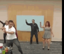 a group of people are dancing in a room in front of a whiteboard .