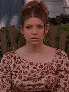 a woman in a floral shirt sits in a wooden chair with her eyes closed