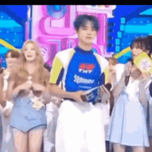 a man in a blue and yellow shirt is standing in front of a group of people on a stage .