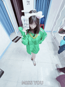 a girl in a green jacket is taking a picture of herself in a dressing room with the words miss you written on the floor