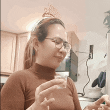 a woman wearing glasses and a birthday crown holds a small cup