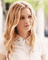 a blonde woman wearing a white shirt with a white collar looks at the camera