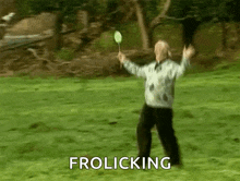 a man is holding a badminton racket in a grassy field with the words frolicking below him .