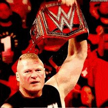 a wrestler is holding a wrestling championship belt over his head .