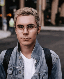 a man wearing glasses and a denim jacket is looking at the camera
