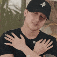 a man wearing a black hat and a black shirt has his hands folded in front of his chest