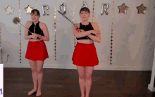 two women in red skirts are standing in front of a wall with roar balloons
