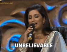 a woman is singing into a microphone and the word unbelievable is on the screen