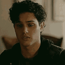 a young man with curly hair and a nose ring is sitting in a chair .