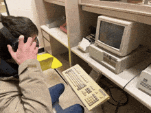 a man talking on a phone while sitting at a desk with a keyboard and a computer monitor