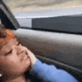 a woman is sleeping in the driver 's seat of a car with her hand on her face .