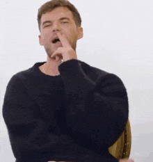 a man in a black sweater is sitting in a chair with his arms crossed and making a funny face .