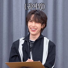 a young man is smiling while holding a clipboard in front of a grey curtain with chinese writing on it