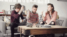 three men are sitting around a table with a bowl on it and the number 2 on the wall