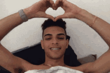 a shirtless man with braces on his teeth makes a heart shape with his hands