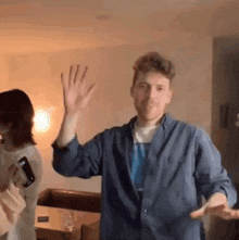 a man in a blue shirt is dancing in a living room while a woman watches .