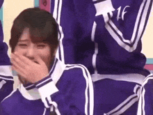 a woman in a purple jacket is covering her mouth with her hand while laughing .