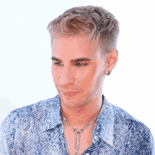 a man with blonde hair wearing a blue shirt and a silver necklace