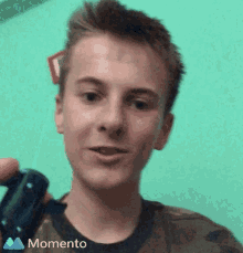 a young man is holding a video game controller and the momento logo can be seen on the bottom of his shirt