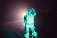 a woman in a white tank top and white shorts stands in the dark