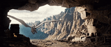 a cave with mountains in the background and a dragon flying through it