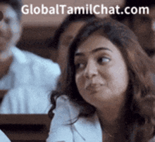 a woman is sitting in a classroom with other people and making a funny face .