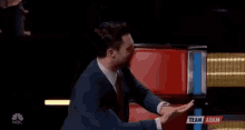a man in a suit and tie is sitting in front of a red chair with his hands outstretched .