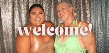 two women standing next to each other with the word welcome behind them
