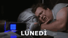 a man is sleeping in a bed next to a clock that says lunedi