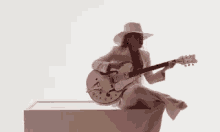 a woman in a cowboy hat is playing a guitar while sitting on a box .